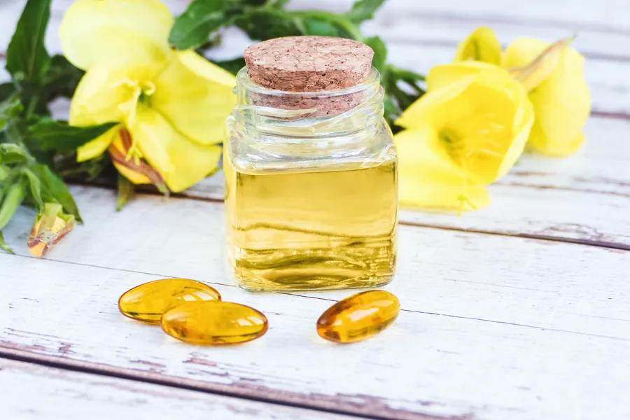 Evening primrose oil in bottle, pills and flowers on wooden table